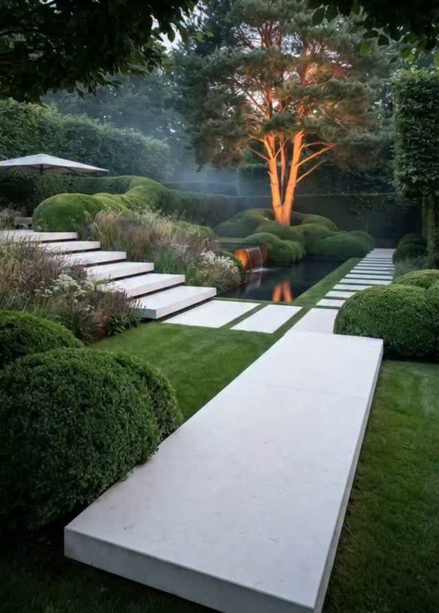 11 Backyard Ideas to Turn Your Outdoor Space Into a Place You Use 2 Illuminated large tree acting as a focal point in a manicured garden with stone pavers.