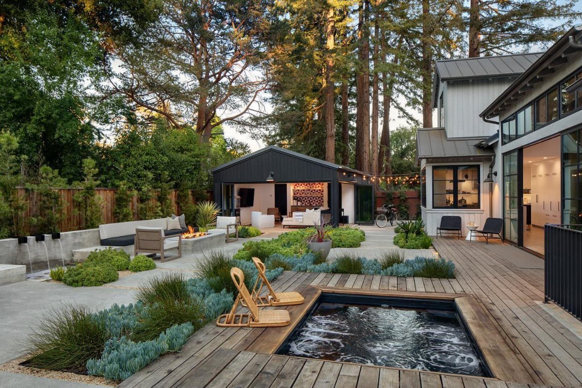 11 Backyard Ideas to Turn Your Outdoor Space Into a Place You Use 7 Modern backyard with a wooden deck, built-in hot tub, and landscaped garden beds near a large house.