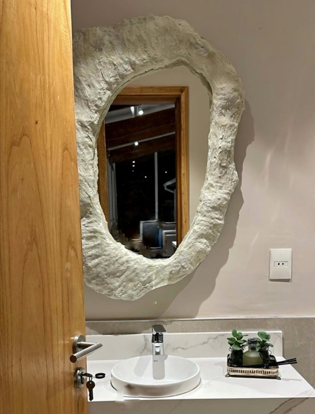 A textured white stone-style mirror hangs above a modern white marble bathroom vanity.