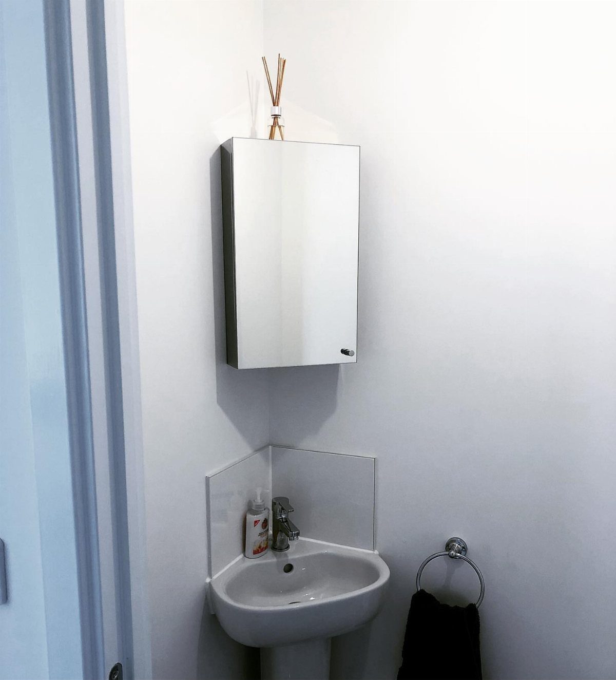 A white corner sink and a rectangular medicine cabinet mounted in a white bathroom corner.