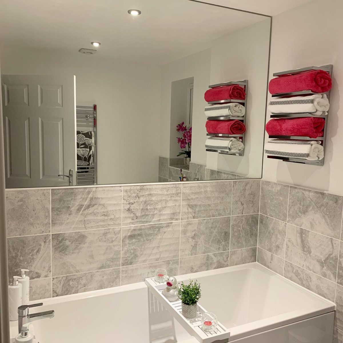 A large rectangular mirror mounted on a white wall above marble tiles and a bathtub.