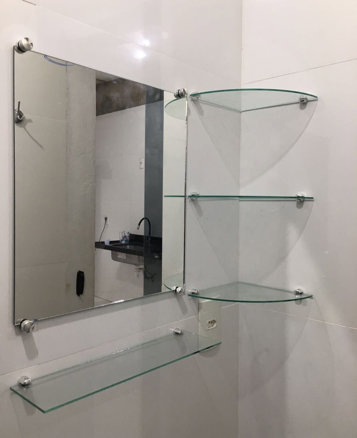 A rectangular mirror mounted on white tiles with several clear glass shelves attached around it.