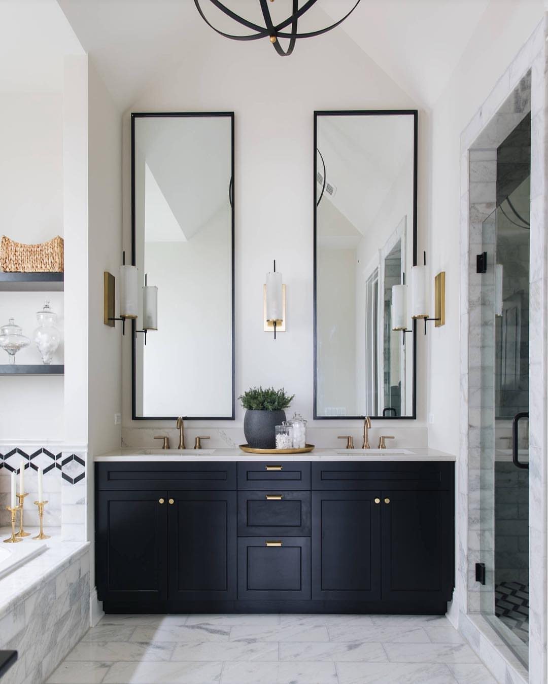 Two tall black-framed mirrors hanging above a dark navy blue bathroom vanity with marble floors.