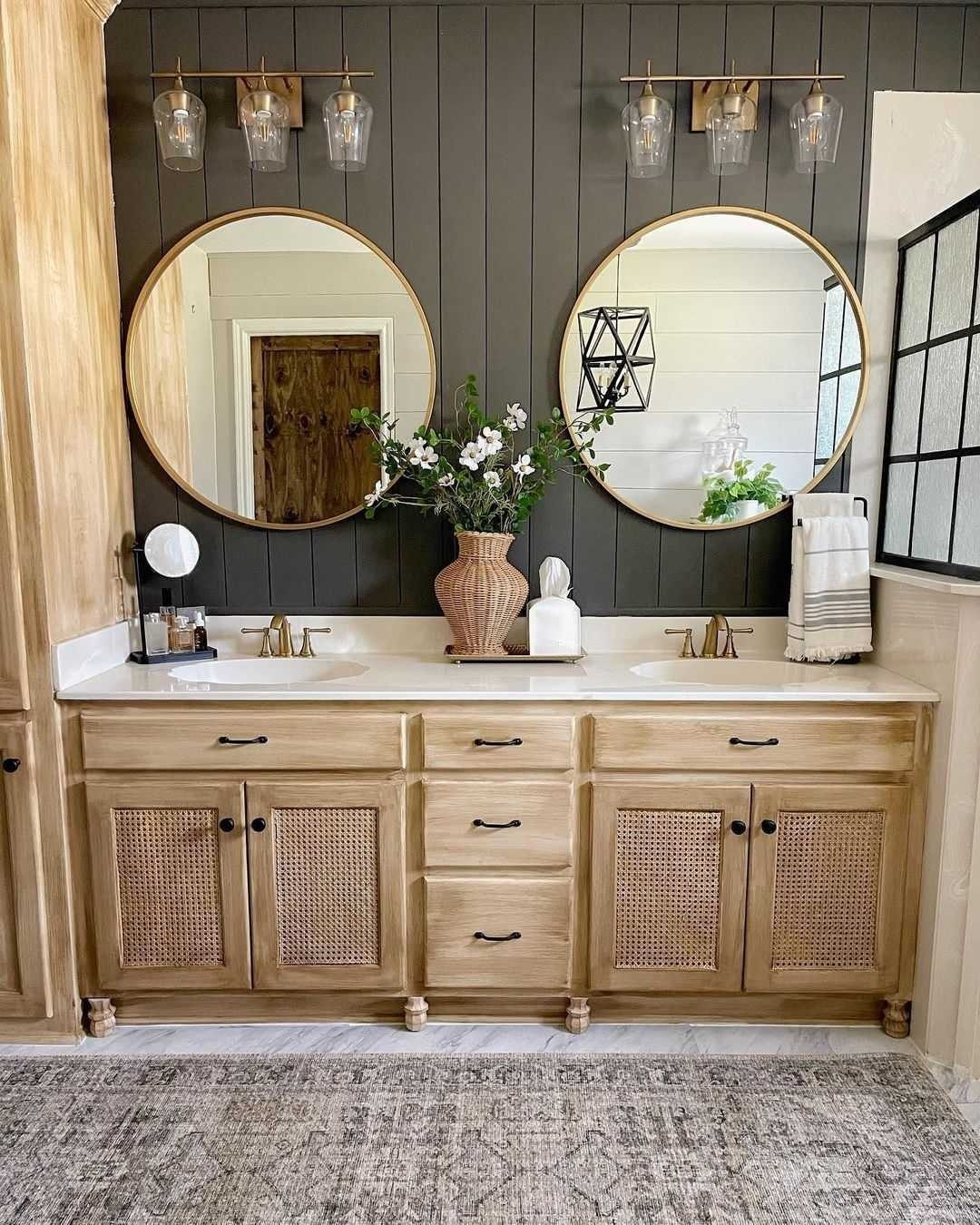 Two round gold-framed mirrors hanging above a light wood vanity with cane cabinet doors.