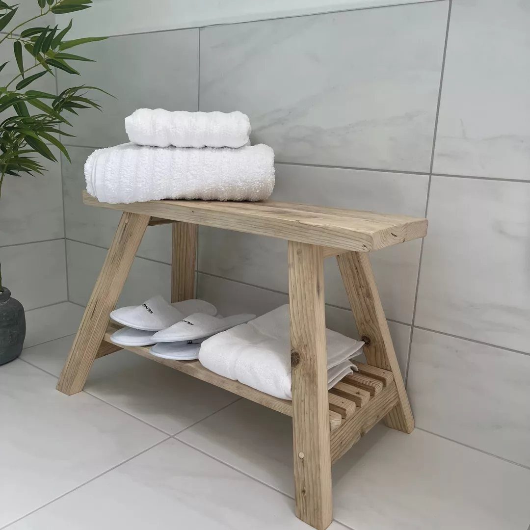 21 Bathroom Shelf Ideas That Make Tight Storage Work Harder 13 Wooden storage bench holding white towels and slippers against marble tiles.