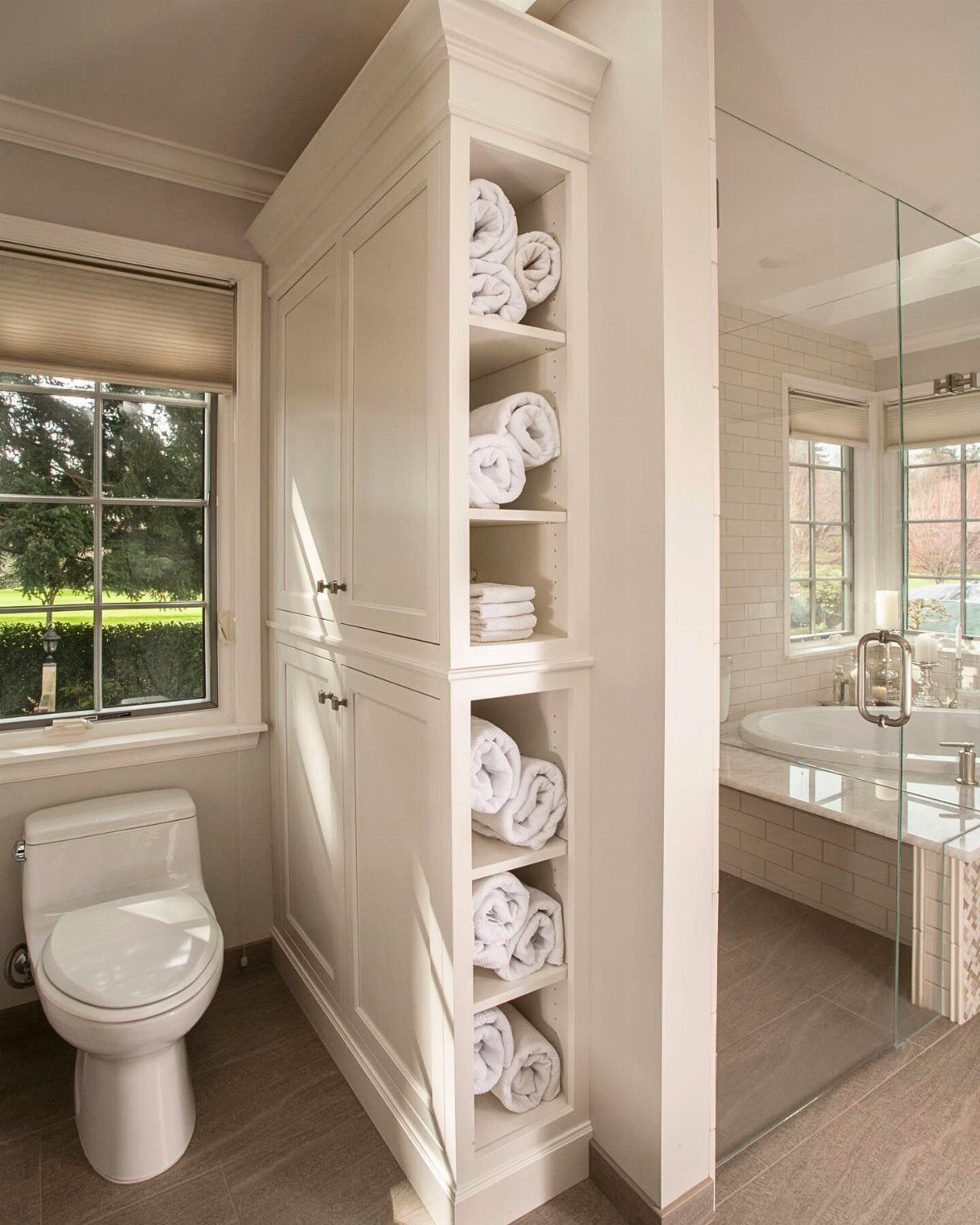 21 Bathroom Shelf Ideas That Make Tight Storage Work Harder 8 White built-in bathroom cabinetry with open shelves holding rolled white towels next to a toilet.
