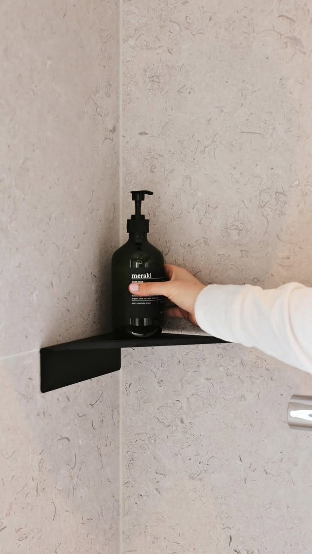21 Bathroom Shelf Ideas That Make Tight Storage Work Harder 10 A hand placing a black soap dispenser onto a black triangular corner shelf in a bathroom.