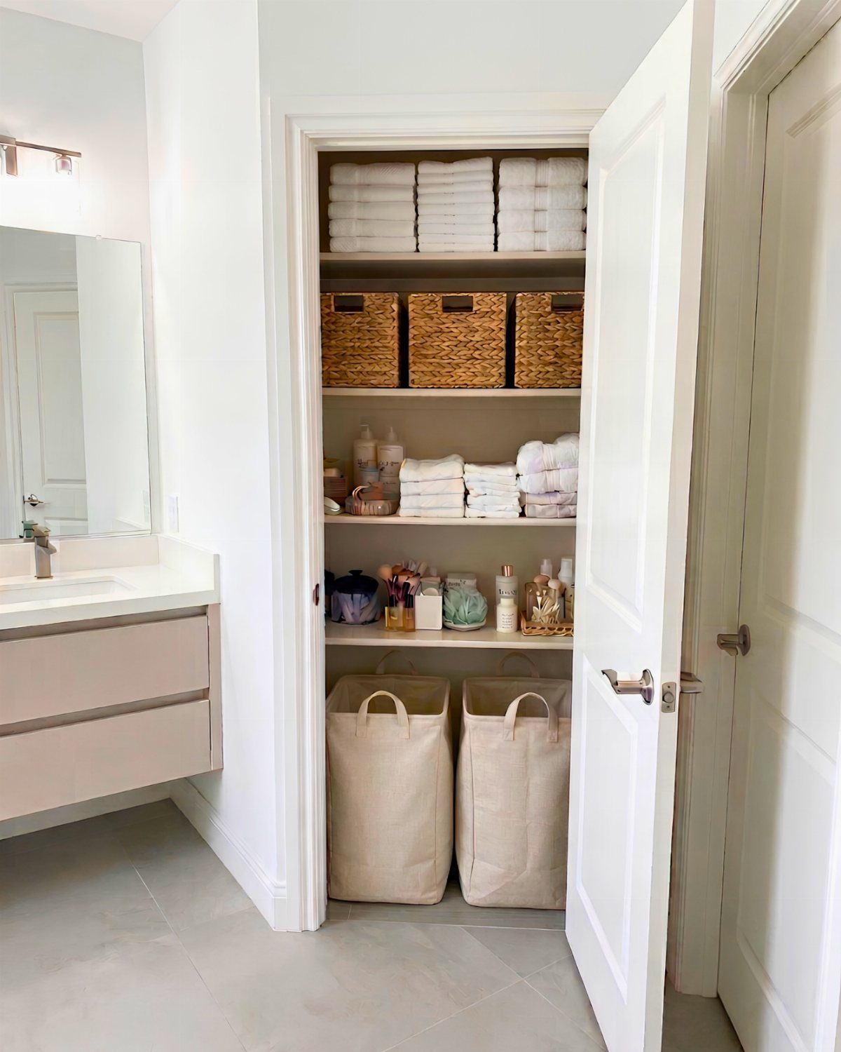 21 Bathroom Shelf Ideas That Make Tight Storage Work Harder 17 White towels and wicker baskets organized on shelves inside an open bathroom closet.