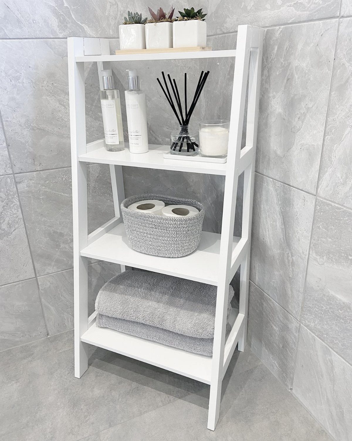 21 Bathroom Shelf Ideas That Make Tight Storage Work Harder 4 White wooden ladder shelf holding bathroom essentials against a grey tiled wall.