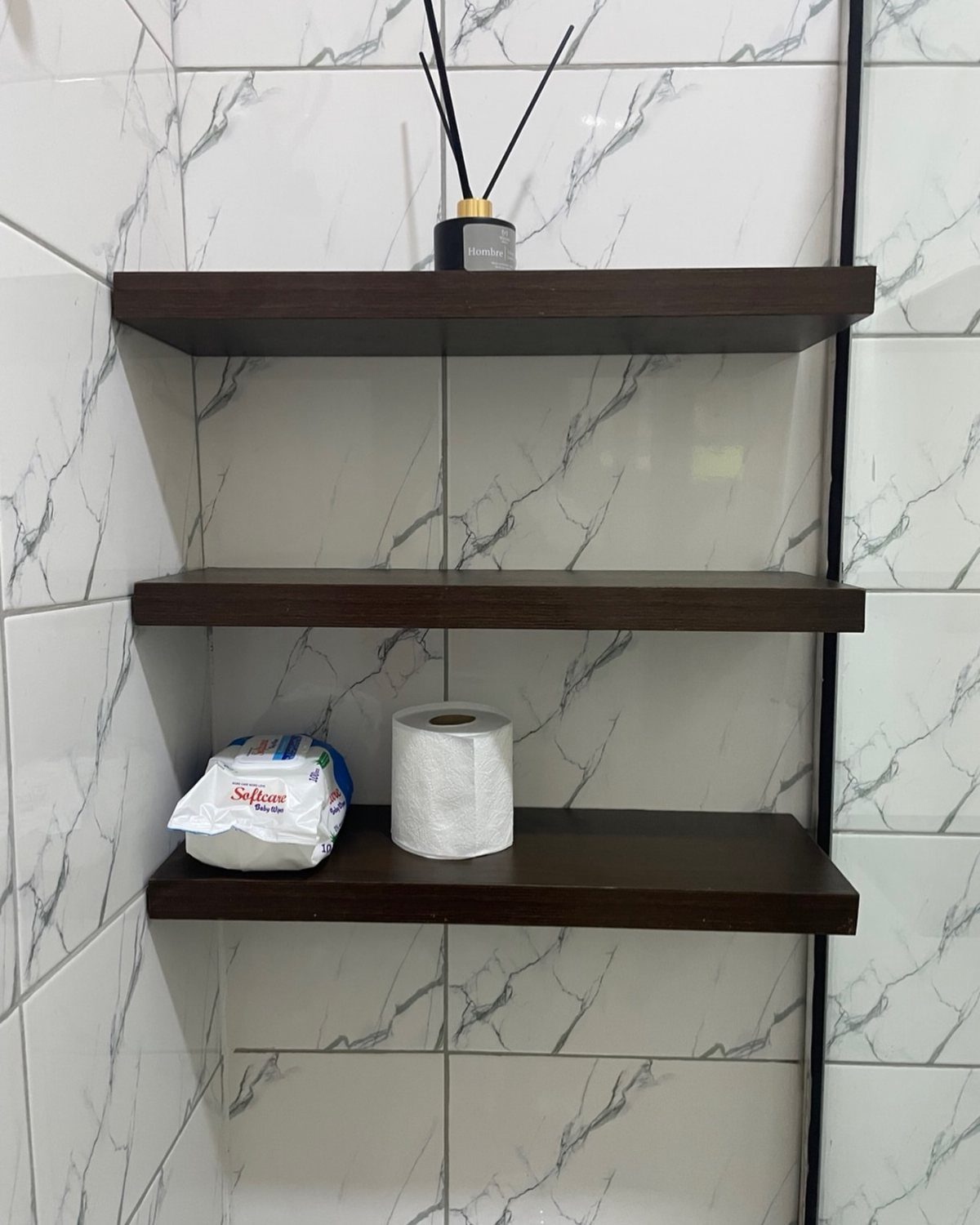 21 Bathroom Shelf Ideas That Make Tight Storage Work Harder 6 Three dark wooden floating shelves mounted on white marble-patterned tiles in a bathroom.