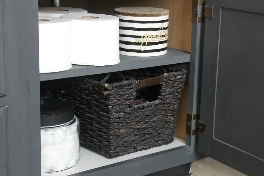 21 Bathroom Shelf Ideas That Make Tight Storage Work Harder 3 Toilet paper, a striped jar, a woven basket, and cotton balls inside a dark grey cabinet.