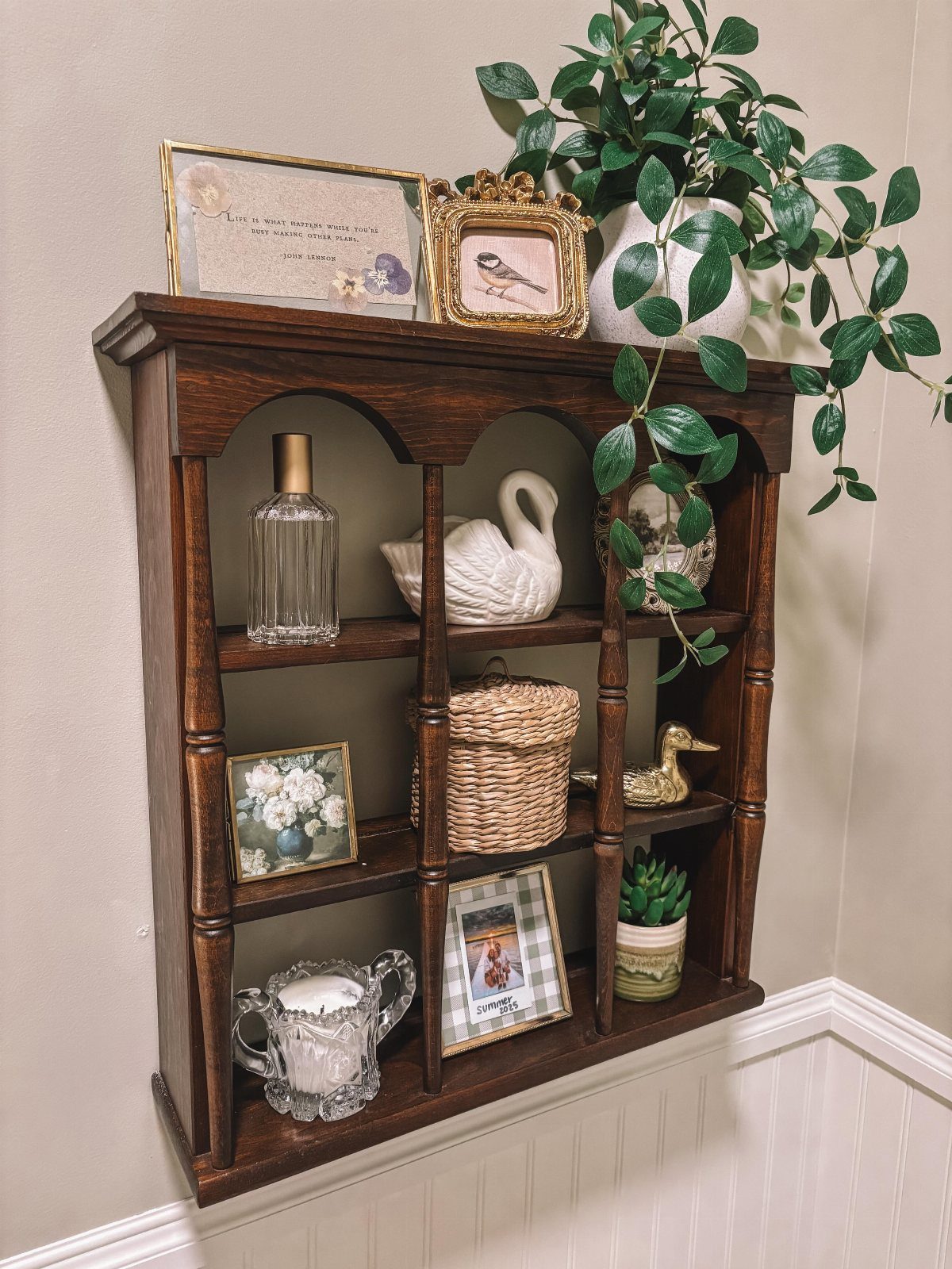 21 Bathroom Shelf Ideas That Make Tight Storage Work Harder 14 Dark wood wall-mounted shelving unit decorated with vintage figurines, baskets, and framed art.