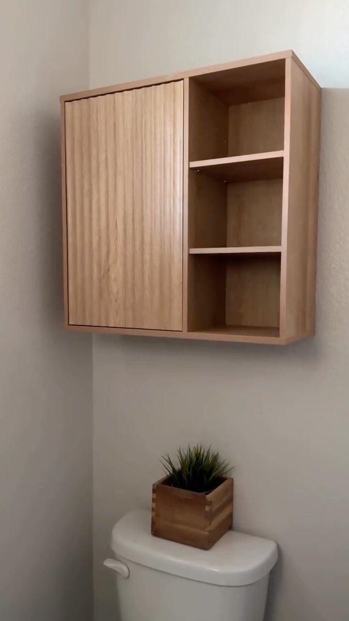 21 Bathroom Shelf Ideas That Make Tight Storage Work Harder 11 Light wood wall-mounted cabinet with a closed door and open cubby shelves above a toilet.
