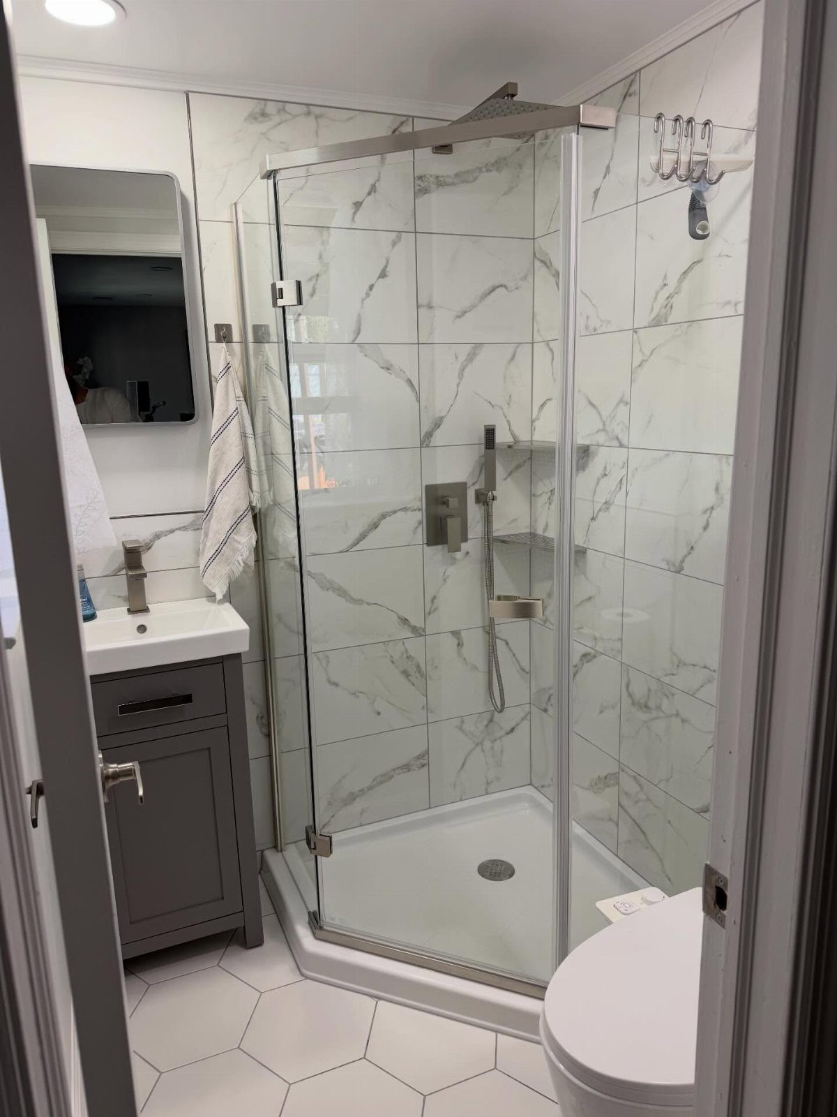 14 Bathroom Shower Ideas, From Rainfall Heads to Wet Rooms 6 A corner walk-in shower with marble tiles and glass doors in a small bathroom.