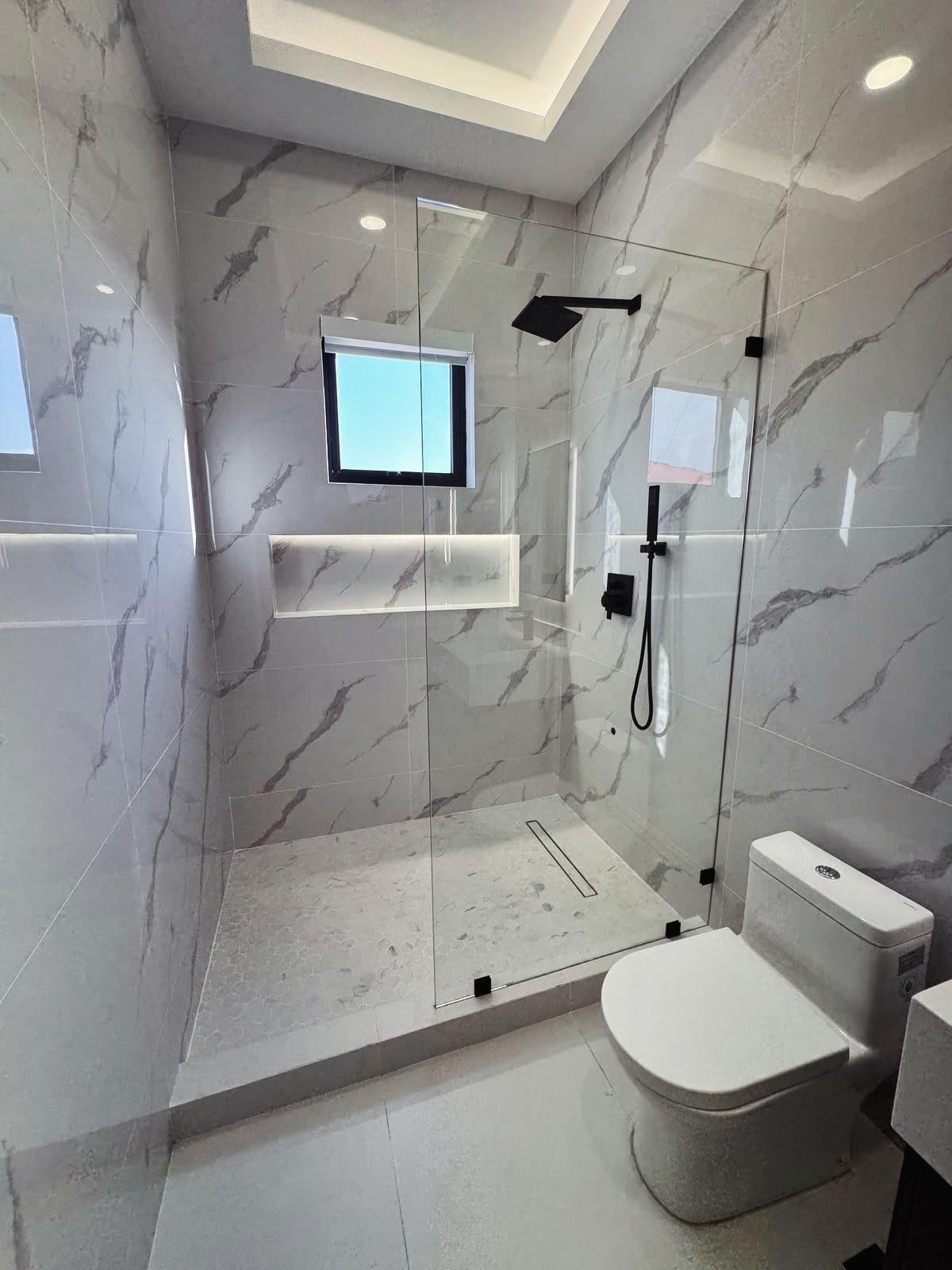 14 Bathroom Shower Ideas, From Rainfall Heads to Wet Rooms 3 Modern bathroom with marble tiles and a frameless glass shower enclosure.