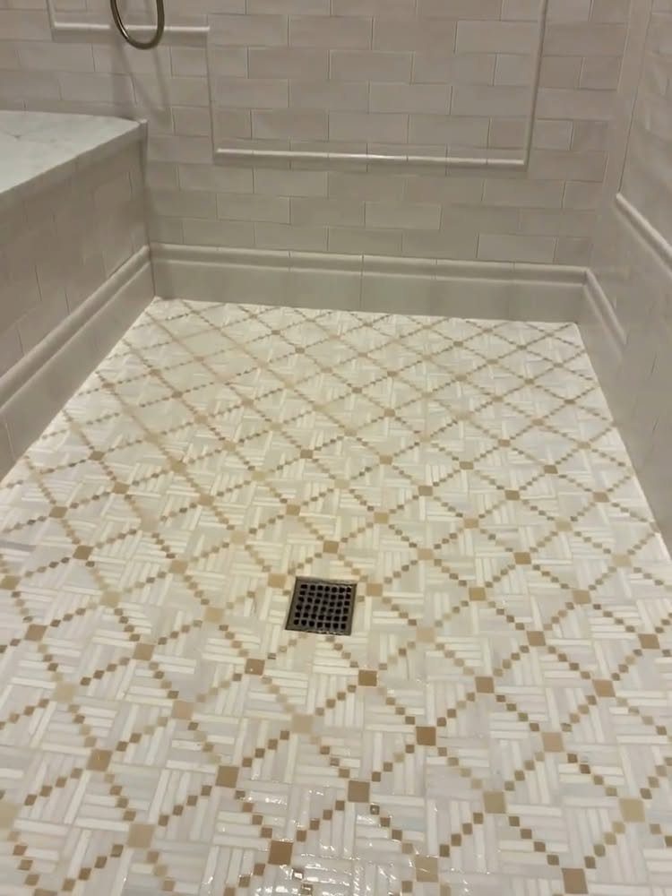 14 Bathroom Shower Ideas, From Rainfall Heads to Wet Rooms 8 Geometric white and tan mosaic tiles covering a bathroom shower floor with a central drain.