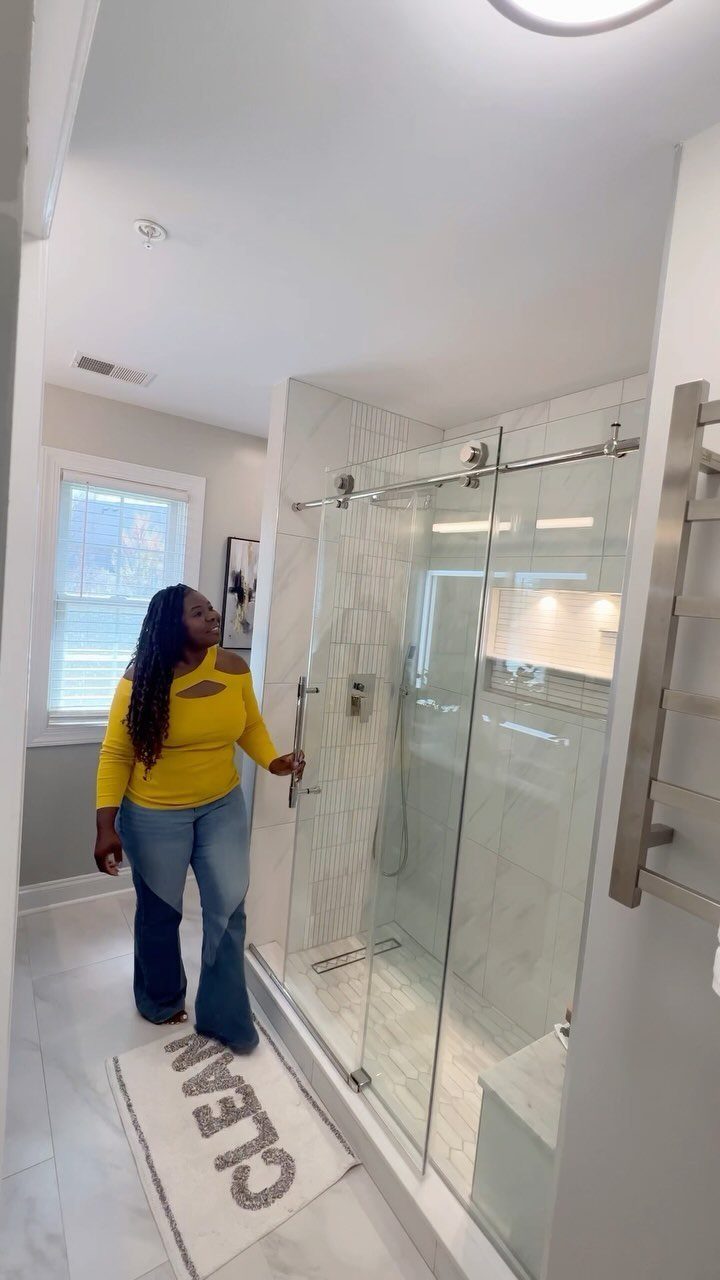 14 Bathroom Shower Ideas, From Rainfall Heads to Wet Rooms 7 A woman standing in a bright bathroom next to a large glass walk-in shower.