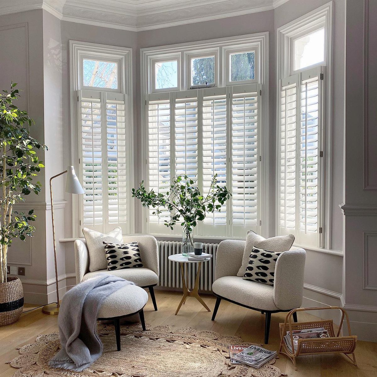 8 Bay Window Ideas for Seating, Dining, Curtains and More 7 Two white armchairs and an ottoman arranged in front of a large bay window.