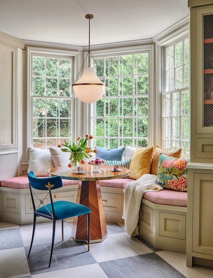 8 Bay Window Ideas for Seating, Dining, Curtains and More 3 A round wooden dining table with blue chairs and cushioned built-in seating inside a bay window.