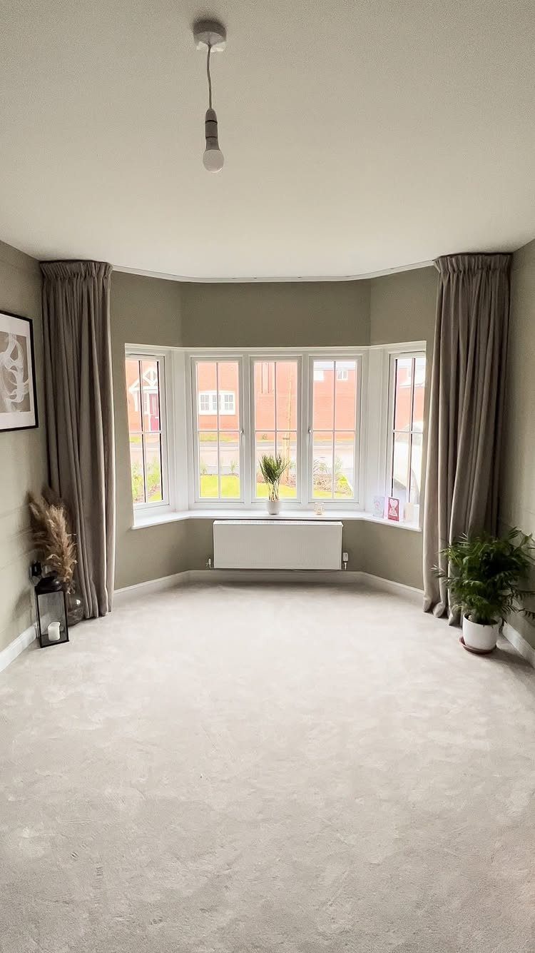 8 Bay Window Ideas for Seating, Dining, Curtains and More 4 Grey floor-length curtains framing a large white bay window in a neutral room.