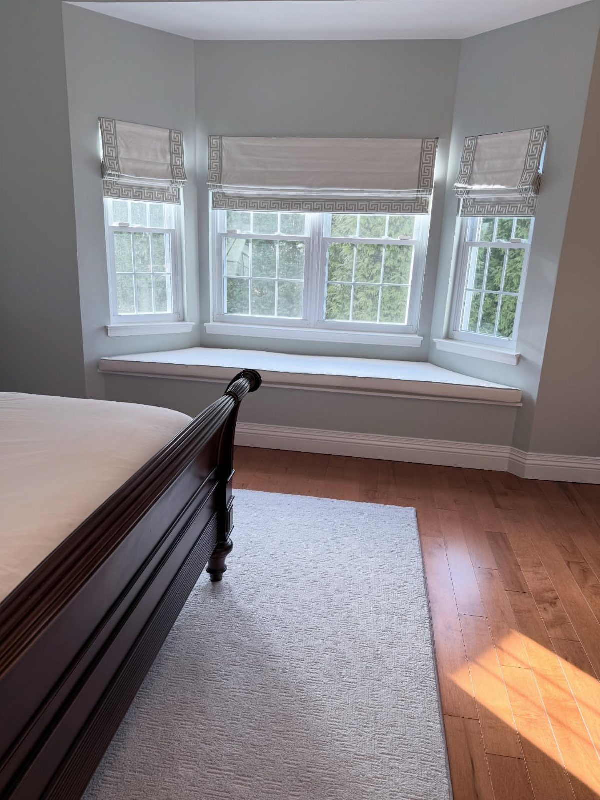 8 Bay Window Treatment Ideas That Balance Light and Privacy 1 Roman shades installed on a three-window bay window above a built-in window seat.