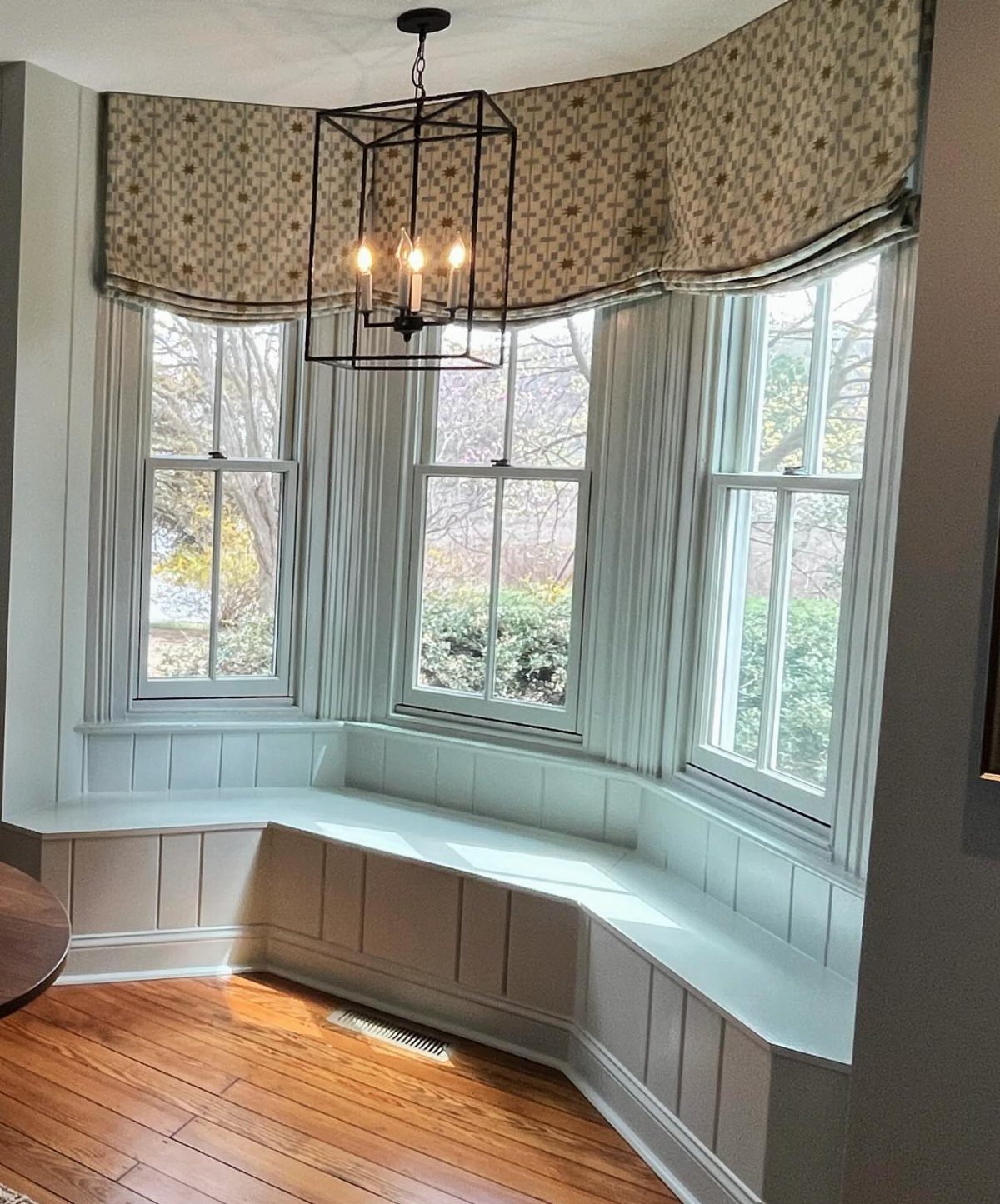 8 Bay Window Treatment Ideas That Balance Light and Privacy 5 Patterned fabric valance hanging above a bay window with a built-in window seat.
