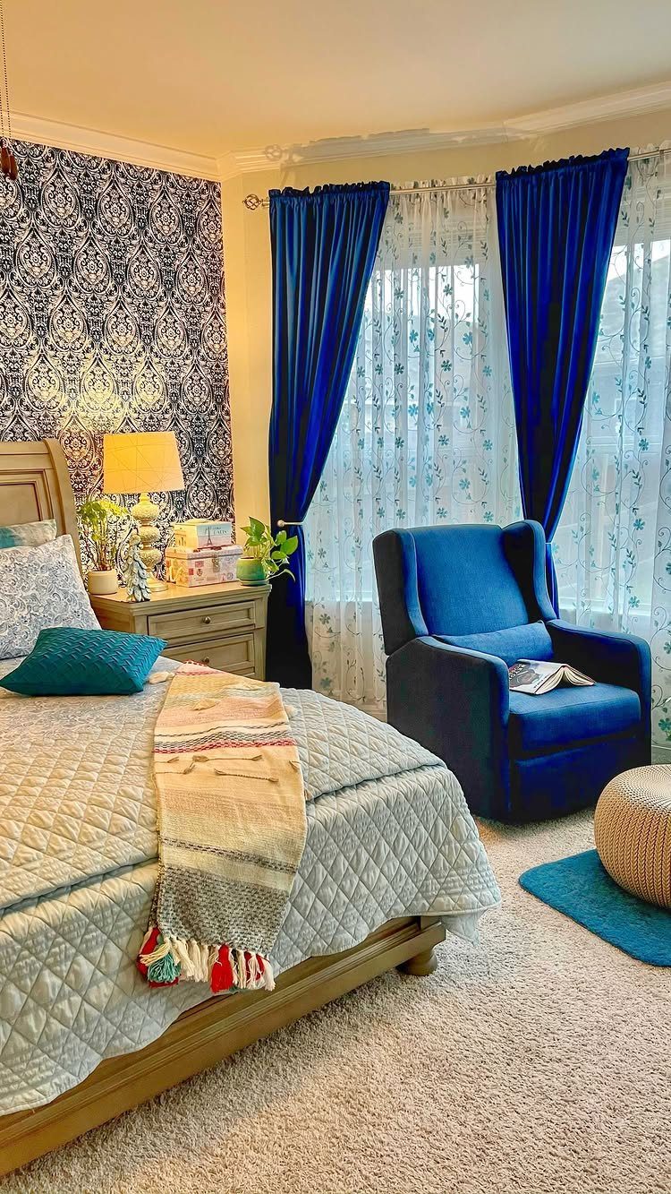 8 Bay Window Treatment Ideas That Balance Light and Privacy 6 Blue velvet curtains hanging beside sheer white window treatments in a bedroom with a blue armchair.