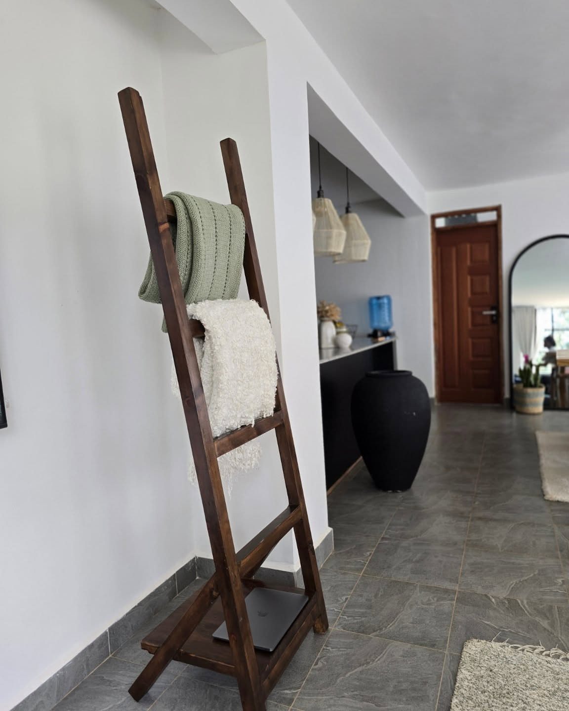 10 Blanket Storage Ideas for Small Spaces and Closets 1 A wooden blanket ladder with green and white blankets draped over its rungs against a white wall.