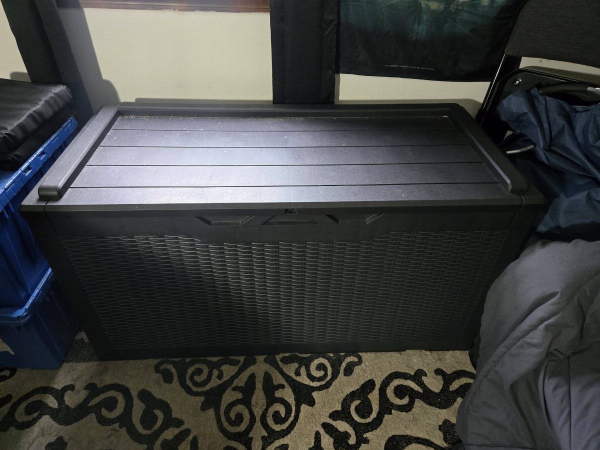 10 Blanket Storage Ideas for Small Spaces and Closets 10 A large black plastic storage trunk sitting on a patterned rug indoors.