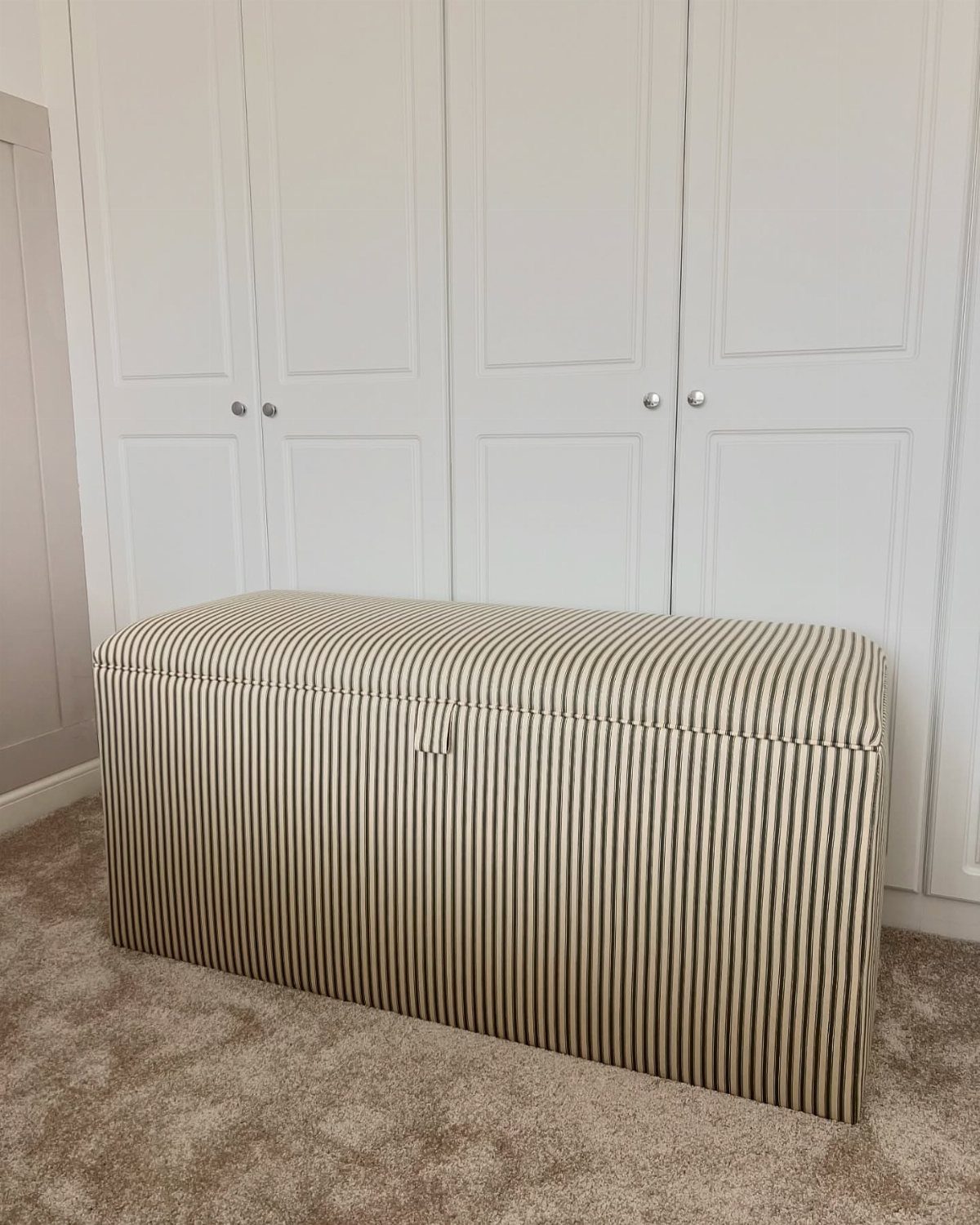 10 Blanket Storage Ideas for Small Spaces and Closets 2 A striped storage ottoman sits on a carpeted floor in front of white closet doors.