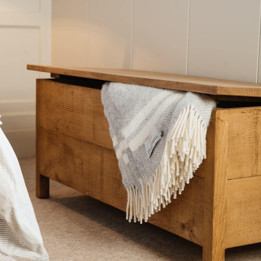 10 Blanket Storage Ideas for Small Spaces and Closets 8 A wooden blanket chest with a grey fringed blanket draped over its open lid.