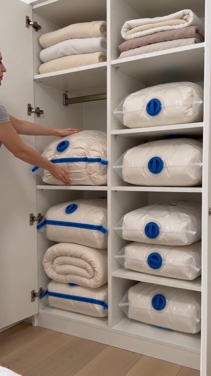 10 Blanket Storage Ideas for Small Spaces and Closets 5 A person organizing white vacuum storage bags filled with blankets on white closet shelves.
