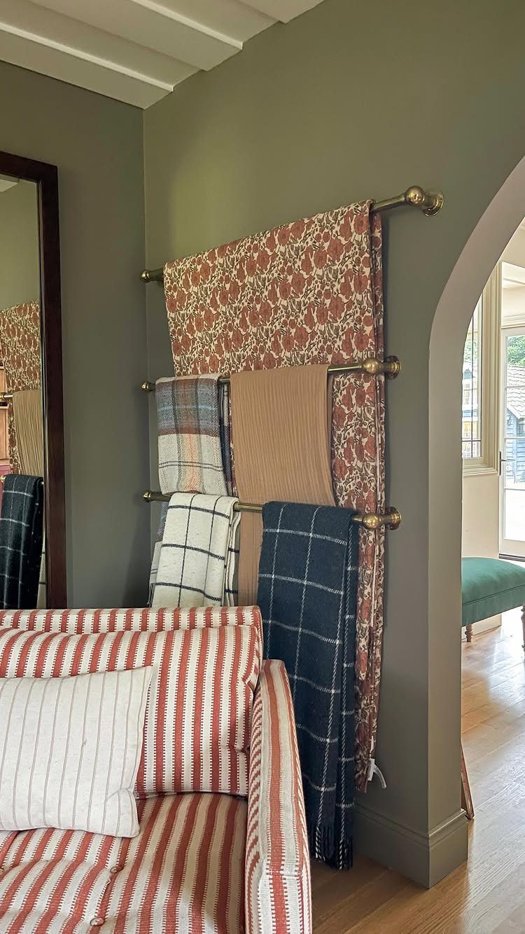 10 Blanket Storage Ideas for Small Spaces and Closets 3 Patterned blankets hanging on brass wall-mounted rods against a green wall.