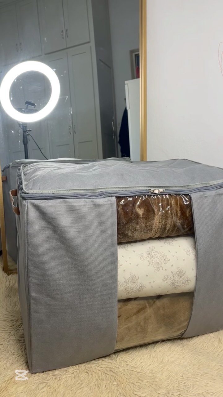 10 Blanket Storage Ideas for Small Spaces and Closets 9 Grey fabric storage bag containing folded blankets sitting on a light carpeted floor.