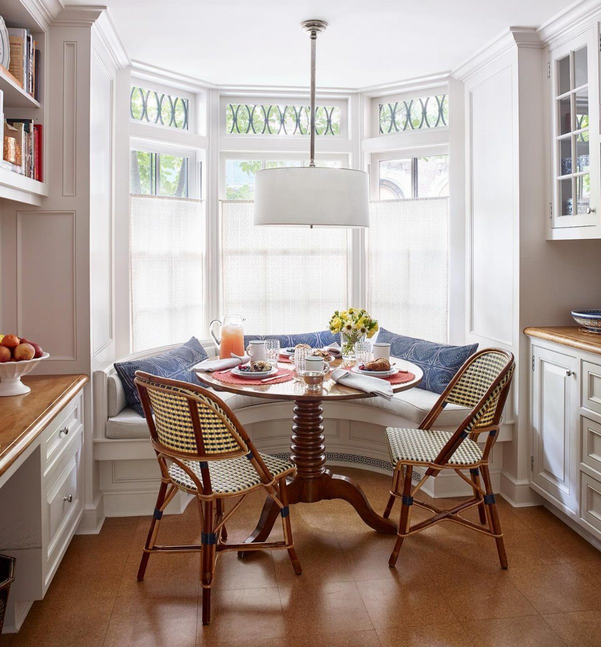 A breakfast nook with a round table and banquette seating inside a bay window.