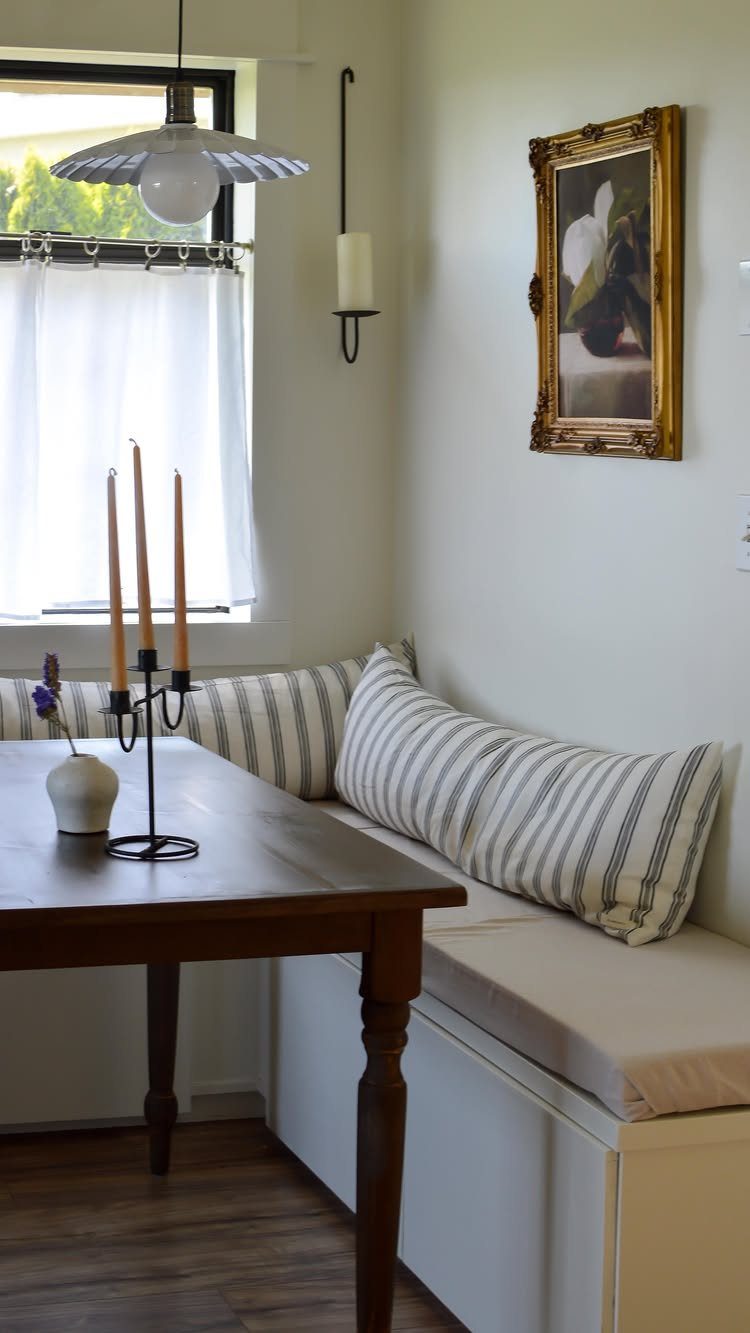 A wooden dining table positioned in front of a white built-in bench with striped pillows.