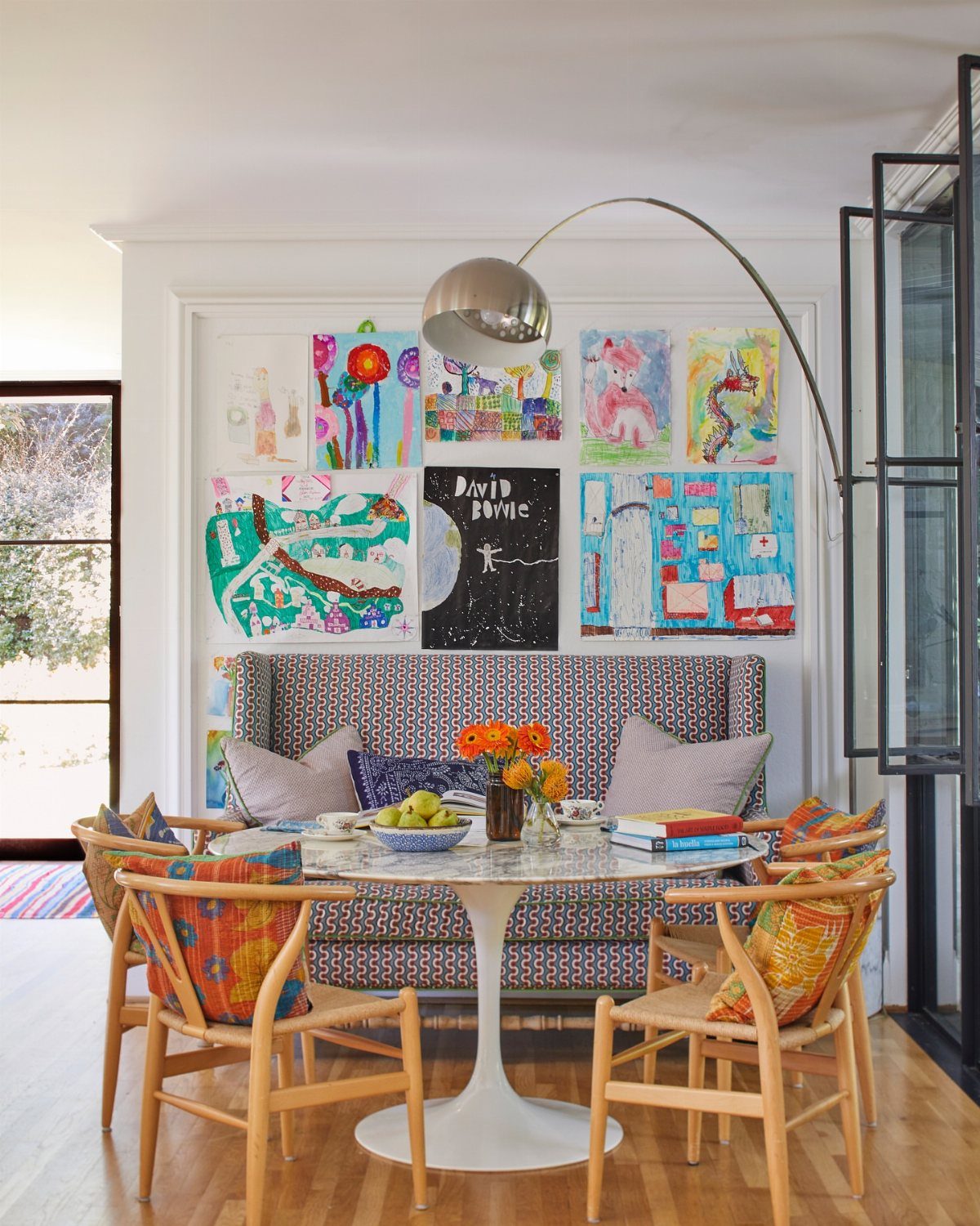 Colorful children's artwork displayed on a white wall above a patterned breakfast nook banquette.
