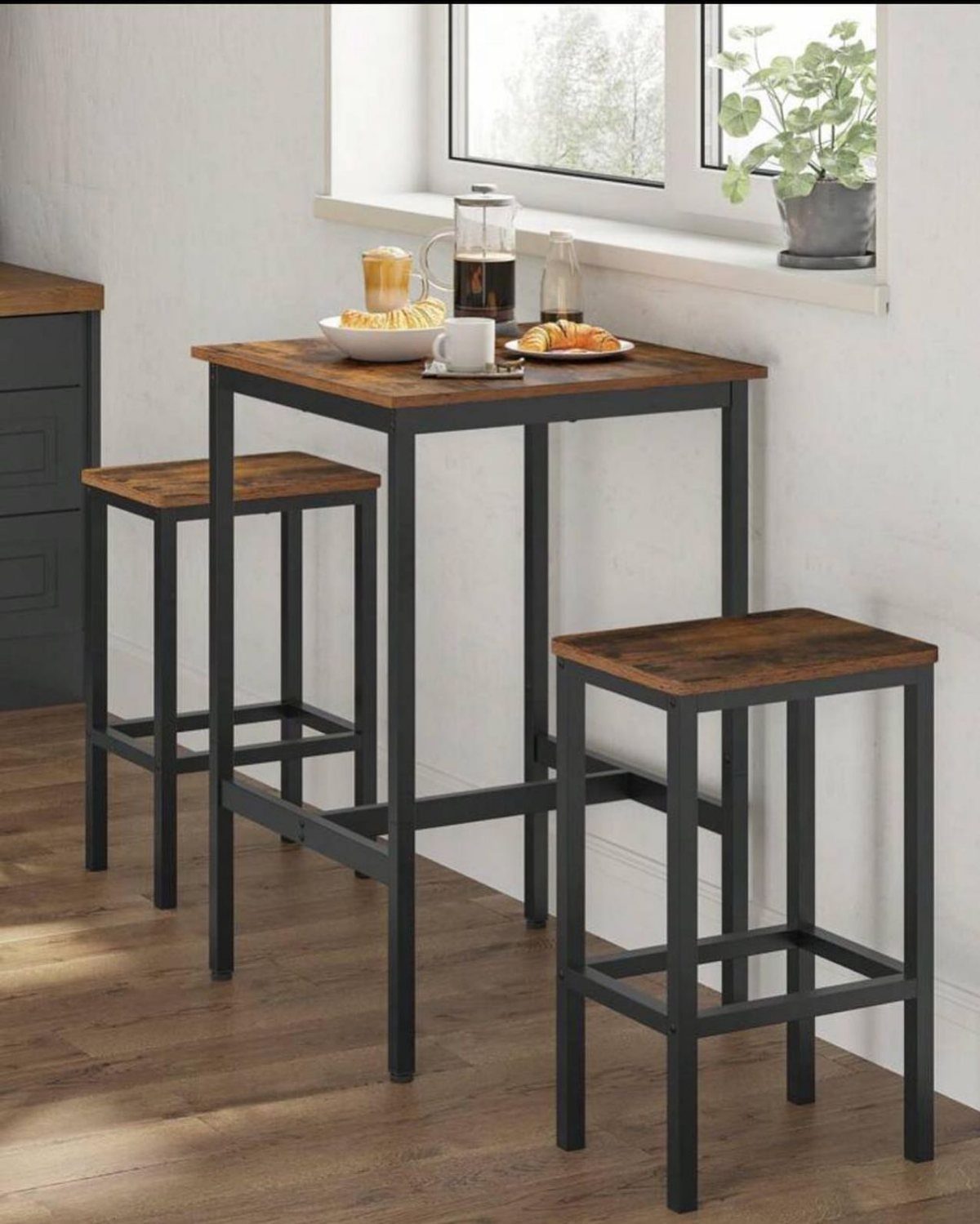A high wooden breakfast table with two matching stools set near a bright window.