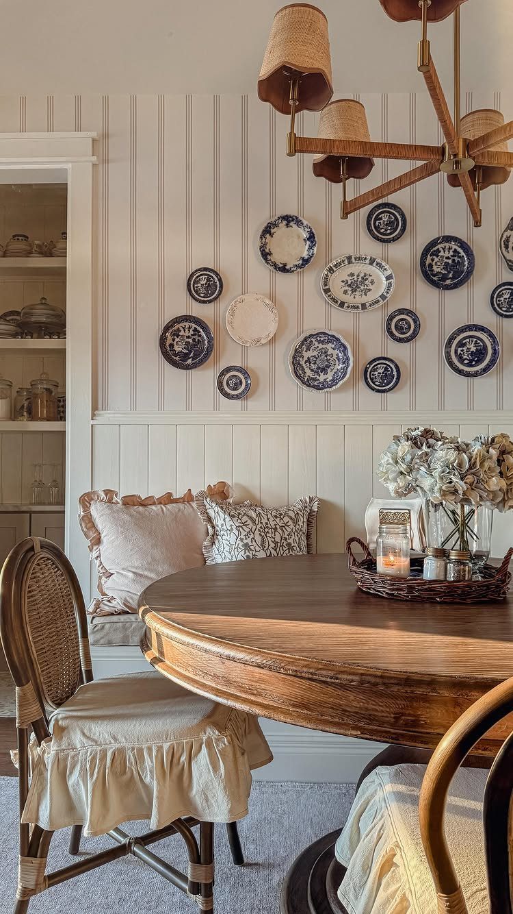 Wooden dining table and cane chairs set against a white beadboard wall decorated with blue patterned plates.