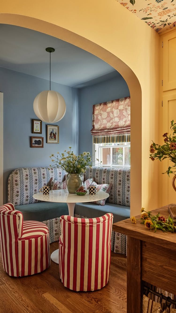 A breakfast nook with a round white table, blue banquette seating, and red striped chairs.