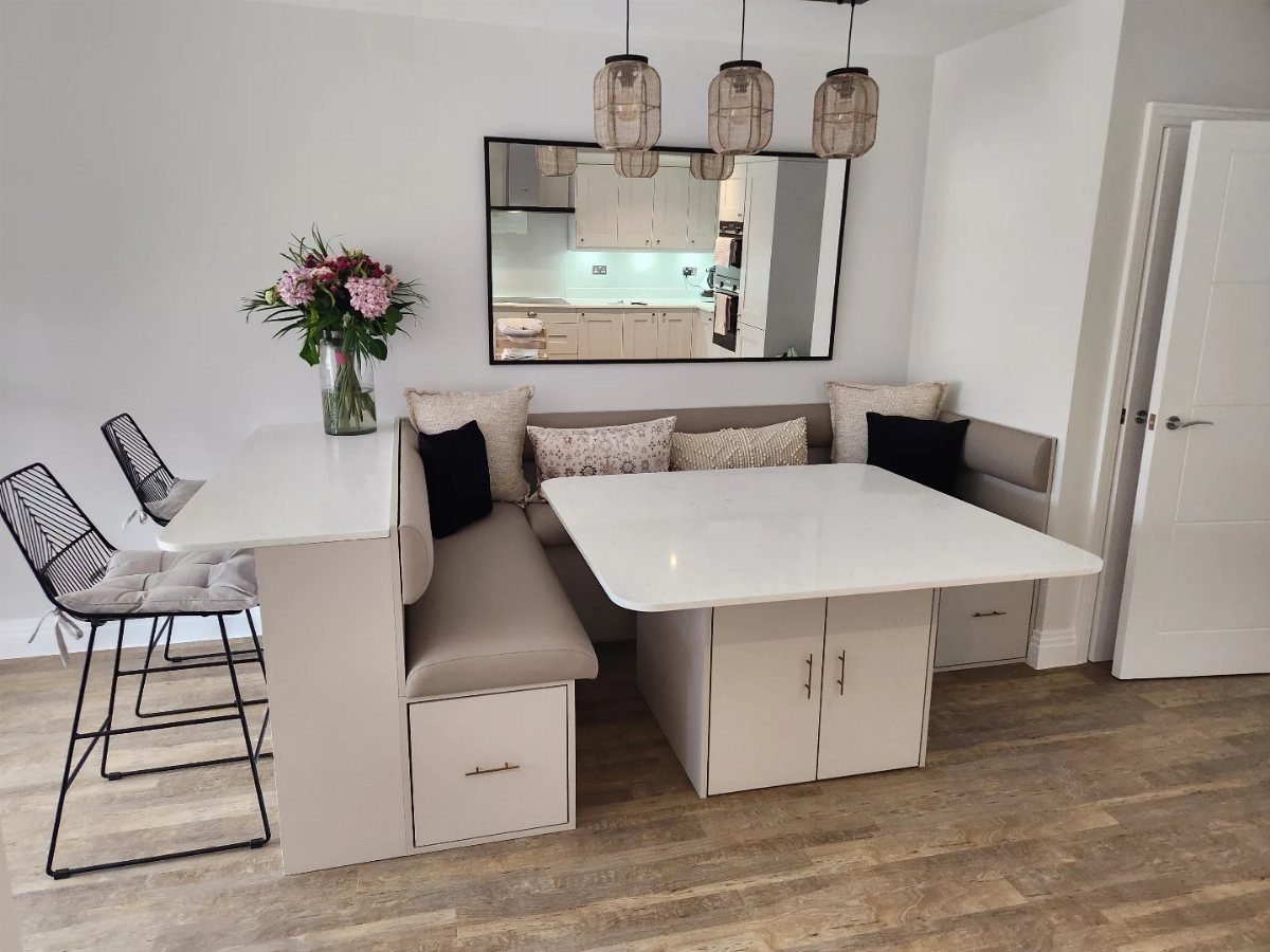Built-in breakfast nook with white table, beige banquette seating, and integrated storage drawers and cabinets.