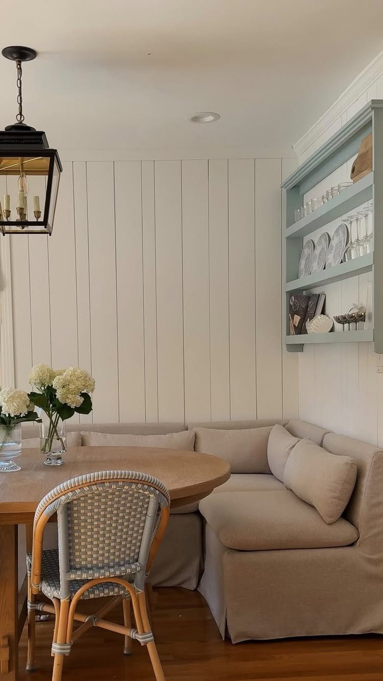 A wooden dining table and beige banquette seating set against white wood paneled walls.