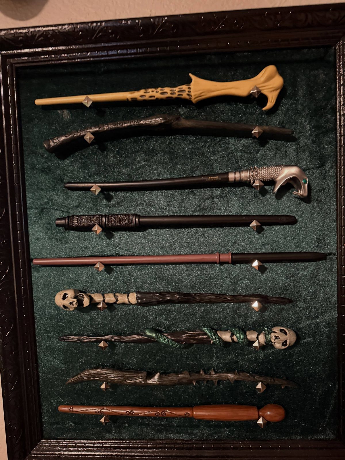 Nine diverse magic wands displayed horizontally inside a dark wooden case with green velvet lining.