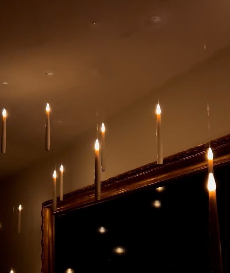 Lit white taper candles hanging from a ceiling by invisible strings above a gold mirror.