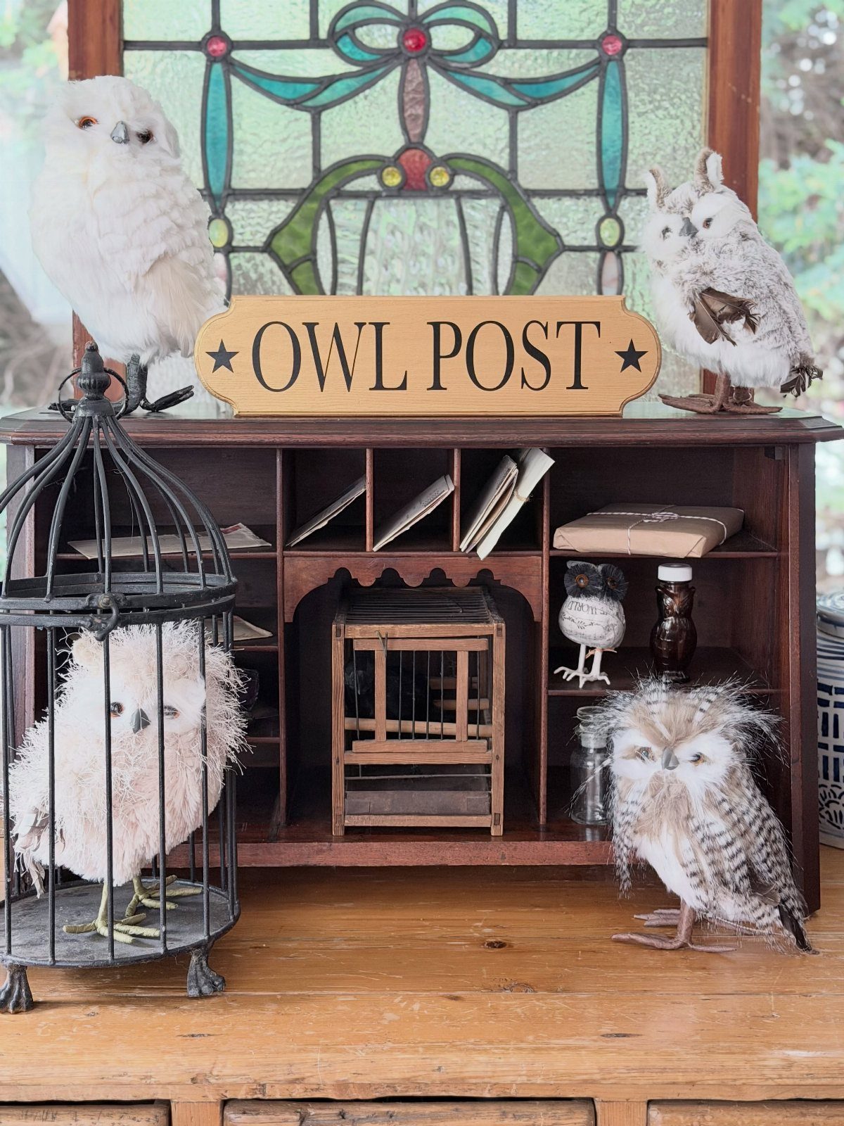 Small owl figurines and a birdcage arranged on a wooden cabinet with an owl post sign.