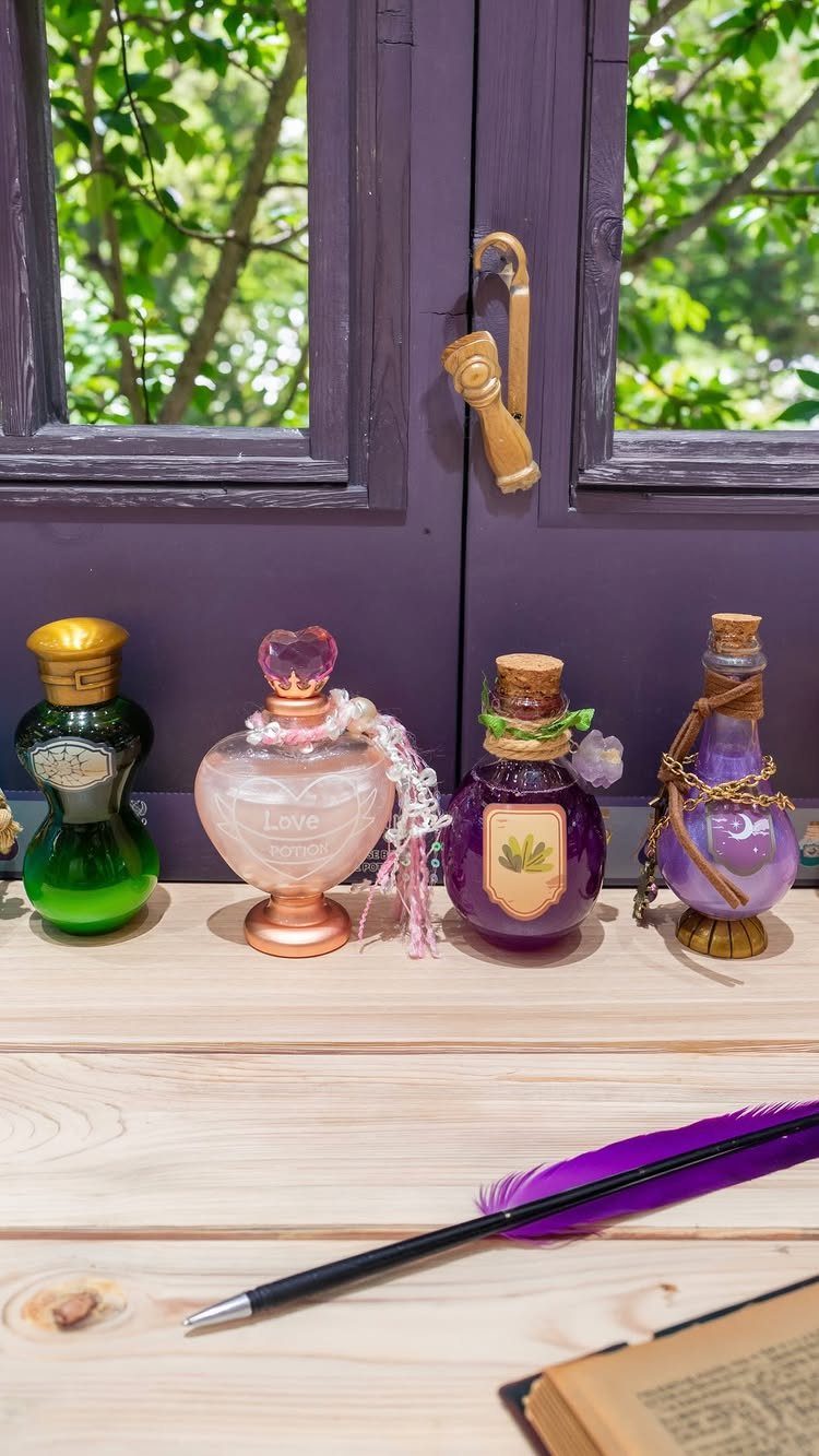 Four colorful decorative glass potion bottles arranged on a wooden surface in front of a purple window.