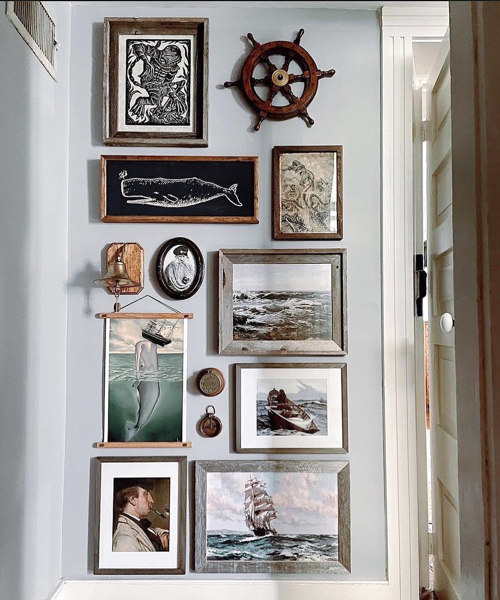 Nautical wall decor featuring framed ocean art, a wooden ship wheel, and a brass bell.