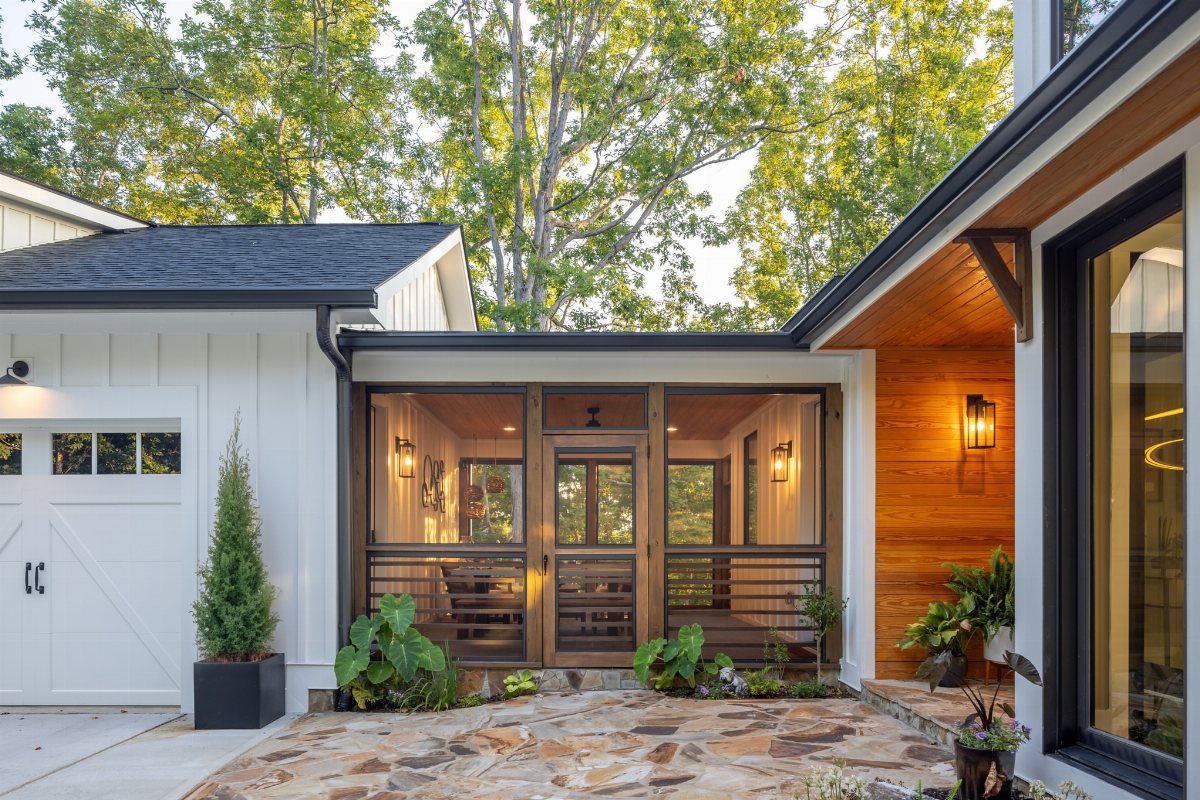 A modern screened-in porch with dark frames and warm lighting attached to a white house.
