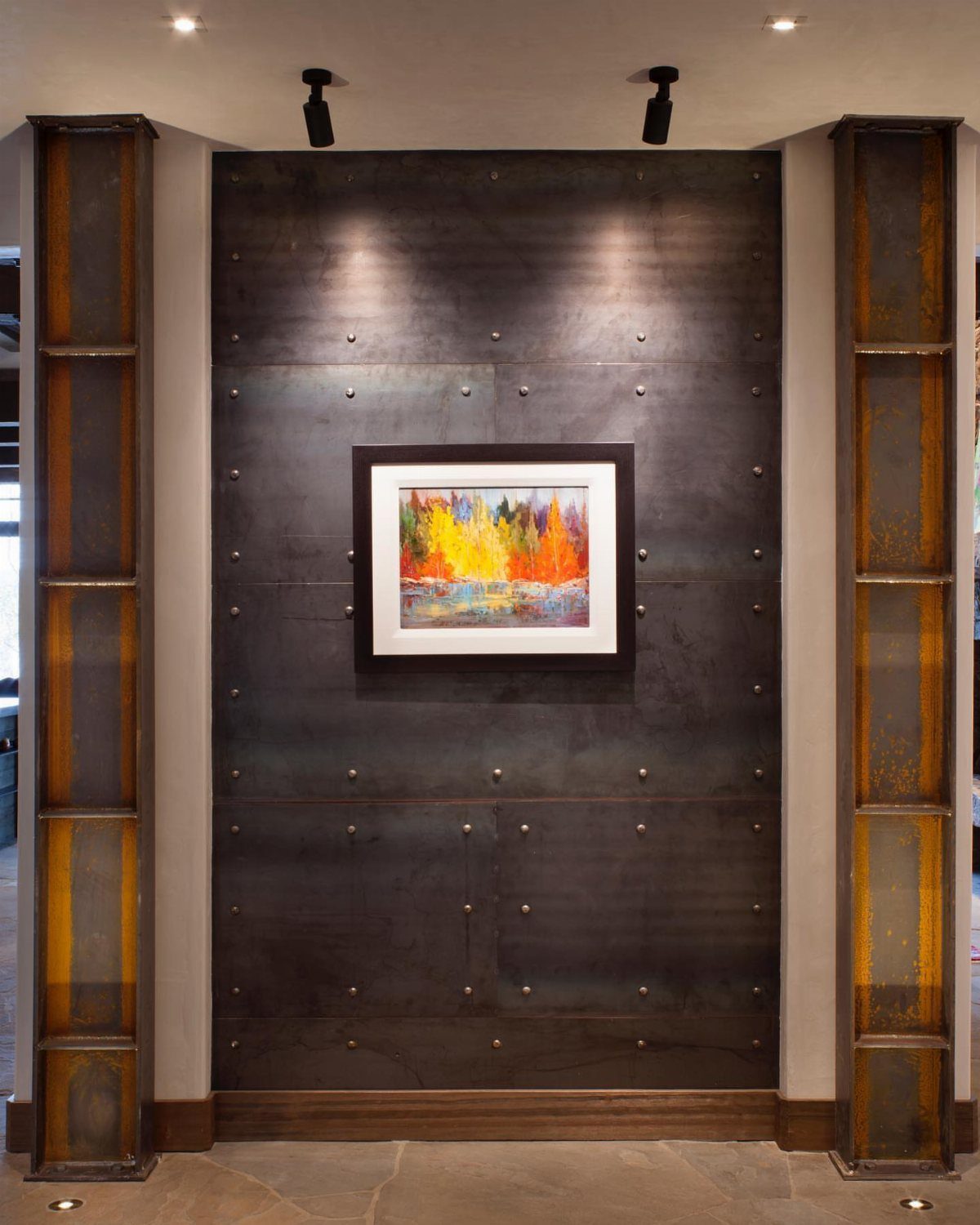 A colorful autumn landscape painting mounted on a dark, industrial metal paneled wall.