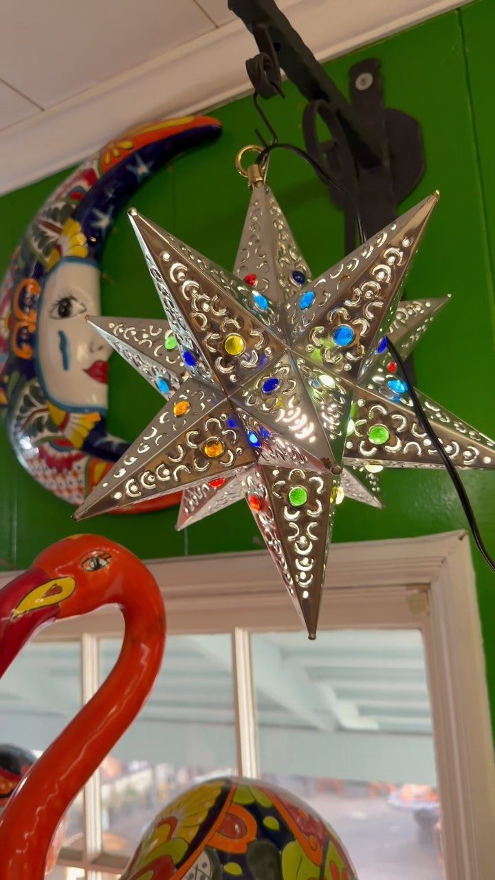 14 Mexican Decor Ideas for Every Room 10 Silver star-shaped lantern with colorful lights hanging against a green wall with colorful decorations.